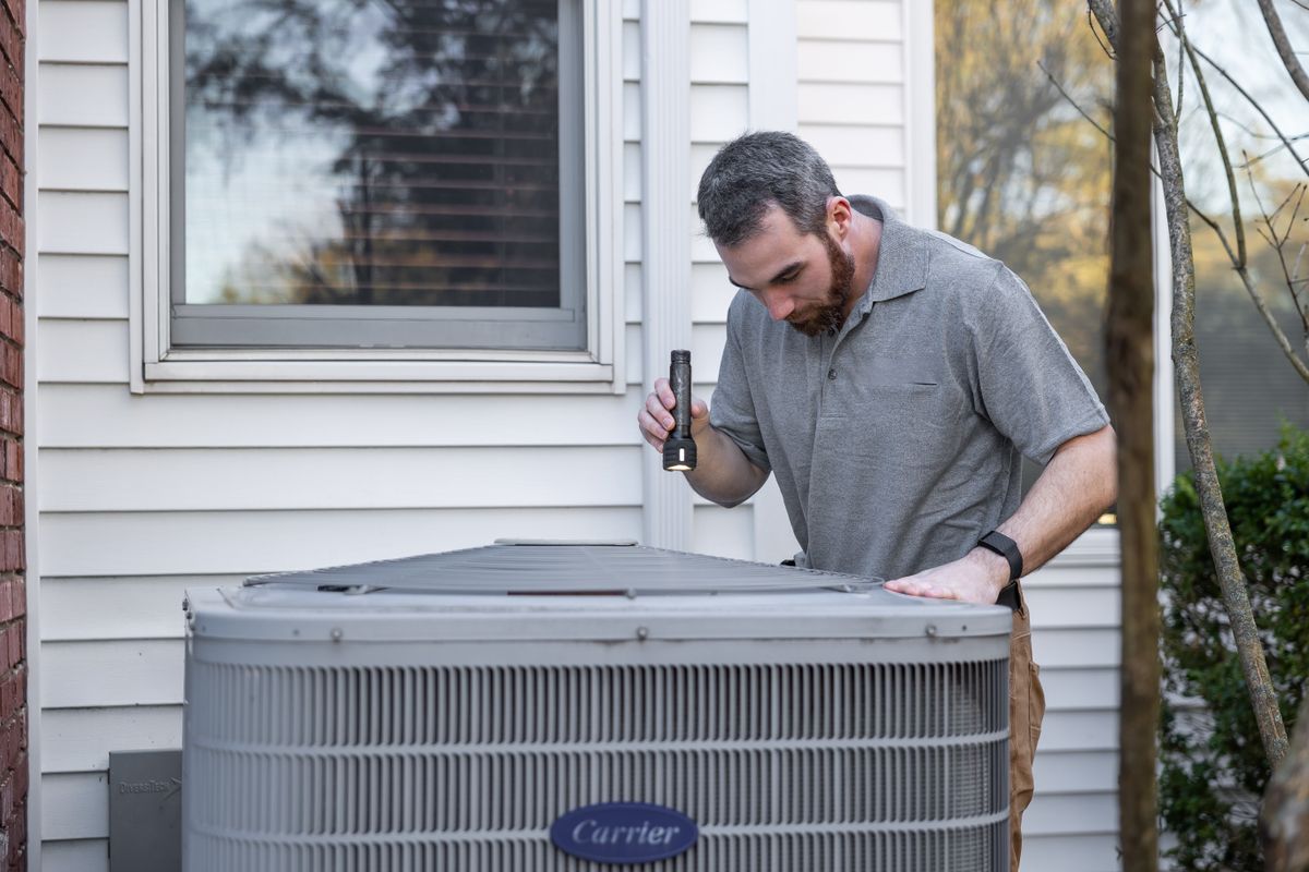 HVAC technician inspecting a rooftop condenser unit with a flashlight
