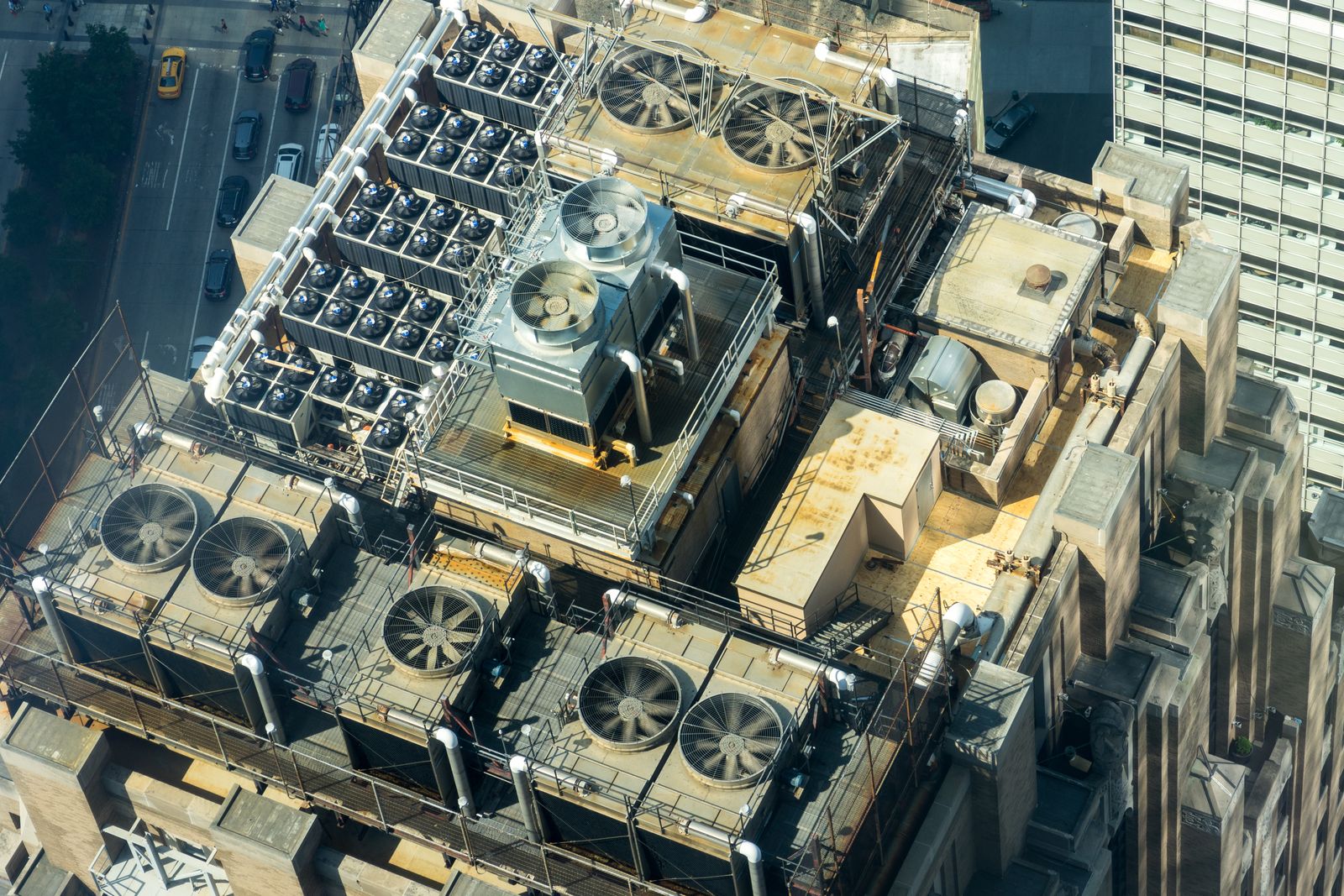 Aerial view of a commercial building rooftop packed with HVAC cooling towers and condenser fan banks in a downtown district