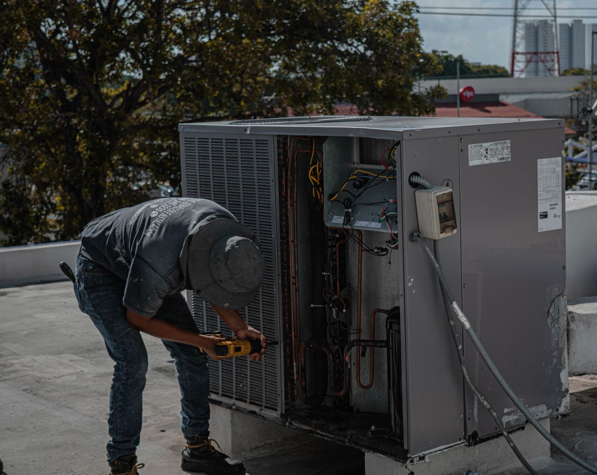 Technician installing and wiring an opened rooftop packaged HVAC unit